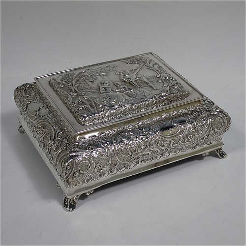 A very pretty Antique Victorian Sterling Silver casket style jewellery dressing table box, having a rectangular shaped casket style body, with hand-chased floral and scroll decoration, a hinged lid with a hand-chased figural scene, a dark green velvet-lined interior, and all sitting on four shell feet. Made by Henry Matthews of Birmingham in 1900. The dimensions of this fine hand-made antique silver dressing table jewellery box are length 16 cms (6.25 inches), width 13.5 cms (5.25 inches), and height 7 cms (2.75 inches).    