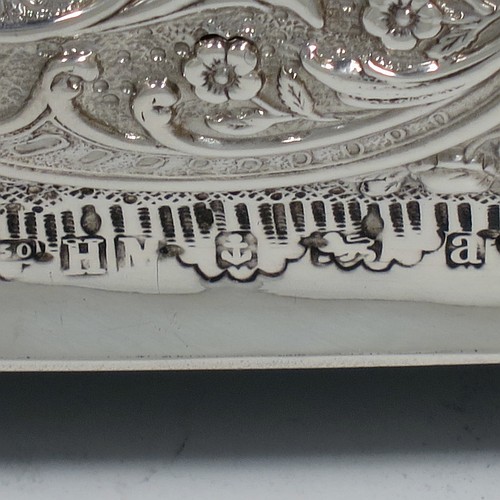 A very pretty Antique Victorian Sterling Silver casket style jewellery dressing table box, having a rectangular shaped casket style body, with hand-chased floral and scroll decoration, a hinged lid with a hand-chased figural scene, a dark green velvet-lined interior, and all sitting on four shell feet. Made by Henry Matthews of Birmingham in 1900. The dimensions of this fine hand-made antique silver dressing table jewellery box are length 16 cms (6.25 inches), width 13.5 cms (5.25 inches), and height 7 cms (2.75 inches).