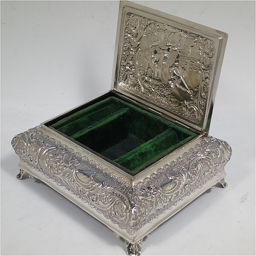 A very pretty Antique Victorian Sterling Silver casket style jewellery dressing table box, having a rectangular shaped casket style body, with hand-chased floral and scroll decoration, a hinged lid with a hand-chased figural scene, a dark green velvet-lined interior, and all sitting on four shell feet. Made by Henry Matthews of Birmingham in 1900. The dimensions of this fine hand-made antique silver dressing table jewellery box are length 16 cms (6.25 inches), width 13.5 cms (5.25 inches), and height 7 cms (2.75 inches).