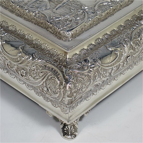A very pretty Antique Victorian Sterling Silver casket style jewellery dressing table box, having a rectangular shaped casket style body, with hand-chased floral and scroll decoration, a hinged lid with a hand-chased figural scene, a dark green velvet-lined interior, and all sitting on four shell feet. Made by Henry Matthews of Birmingham in 1900. The dimensions of this fine hand-made antique silver dressing table jewellery box are length 16 cms (6.25 inches), width 13.5 cms (5.25 inches), and height 7 cms (2.75 inches).