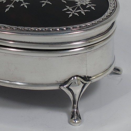 A very pretty Antique Sterling Silver and tortoise-shell jewellery box, having an oval shaped body, a tortoise-shell hinged lid with in-laid flowers and ribbon bows, an applied floral border, a light brown velvet-lined interior, and sitting on four cast foliate legs. Made by Synter and Beddoes of Birmingham in 1912. The dimensions of this fine hand-made antique silver and tortoise-shell jewelery box are length 9.5 cms (3.75 inches), width 6.5 cms (2.5 inches), and height 5 cms (2 inches).
