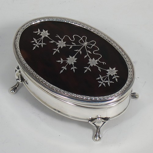 A very pretty Antique Sterling Silver and tortoise-shell jewellery box, having an oval shaped body, a tortoise-shell hinged lid with in-laid flowers and ribbon bows, an applied floral border, a light brown velvet-lined interior, and sitting on four cast foliate legs. Made by Synter and Beddoes of Birmingham in 1912. The dimensions of this fine hand-made antique silver and tortoise-shell jewelery box are length 9.5 cms (3.75 inches), width 6.5 cms (2.5 inches), and height 5 cms (2 inches).