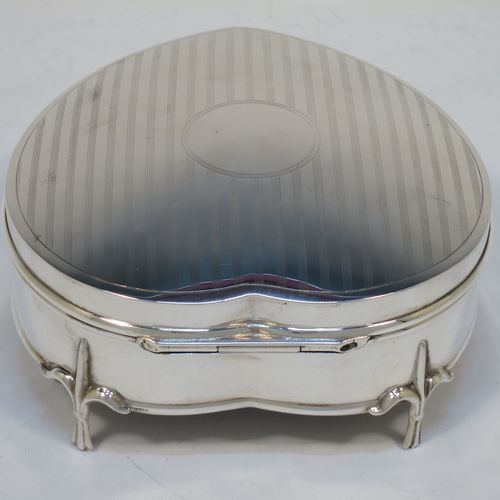 A pretty Antique Sterling Silver jewellery box, having a heart-shaped body with straight sides, a a hinged lid with reeded decoration and a central round vacant cartouche, a gold-gilt and dark-blue velvet-lined interior, and all sitting on three cast fleur-de-lis legs. Made by Saunders and Shepherd of Birmingham in 1918. The dimensions of this fine hand-made antique silver  jewelery box are length 12 cms (4.75 inches), width 11 cms (4.3 inches), and height 5 cms (2 inches).  