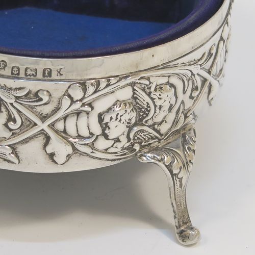 A very beautiful Antique Edwardian Silver jewelery box, having a round body with straight sides and hand-chased floral and cherub face decoration, a hinged lid with a group of hand-chased Seraphims, a gold gilt and dark-blue velvet and satin-lined interior, and all sitting on four cast cabriolet feet. This pretty antique silver jewellery box was made by Deakin and Francis of Birmingham in 1905. The dimensions of this fine hand-made antique silver jewellery box are diameter 11 cms (4.25 inches), and height 6 cms (2.25 inches)