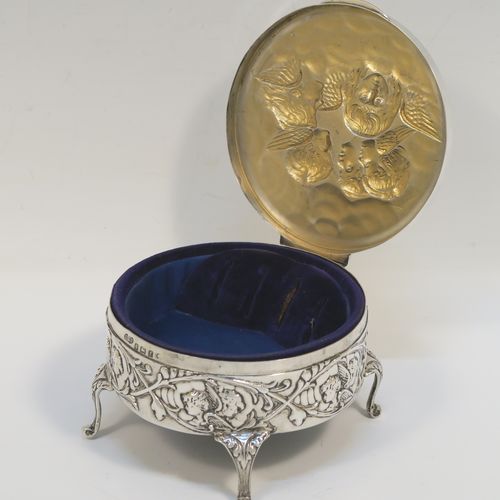 A very beautiful Antique Edwardian Silver jewelery box, having a round body with straight sides and hand-chased floral and cherub face decoration, a hinged lid with a group of hand-chased Seraphims, a gold gilt and dark-blue velvet and satin-lined interior, and all sitting on four cast cabriolet feet. This pretty antique silver jewellery box was made by Deakin and Francis of Birmingham in 1905. The dimensions of this fine hand-made antique silver jewellery box are diameter 11 cms (4.25 inches), and height 6 cms (2.25 inches)