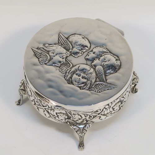 A very beautiful Antique Edwardian Silver jewelery box, having a round body with straight sides and hand-chased floral and cherub face decoration, a hinged lid with a group of hand-chased Seraphims, a gold gilt and dark-blue velvet and satin-lined interior, and all sitting on four cast cabriolet feet. This pretty antique silver jewellery box was made by Deakin and Francis of Birmingham in 1905. The dimensions of this fine hand-made antique silver jewellery box are diameter 11 cms (4.25 inches), and height 6 cms (2.25 inches)