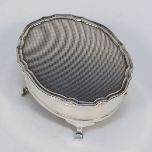 A small but elegant Sterling Silver jewelery box, having a plain oval-shaped body with straight sides, a slightly domed hinged lid with an applied Chippendale border and engine-turned engraved decoration, a gold gilt and red velvet-lined interior, and all sitting on four flanged feet. This beautiful silver jewellery box was made by the Adie Brothers of Birmingham in 1962. The dimensions of this fine hand-made antique silver jewellery box are length 7.5 cms (3 inches), width 6 cms (2.3 inches), and height 4 cms (1.5 inches)