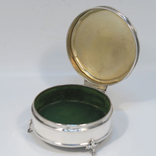 A very handsome Antique Sterling Silver jewelery box, having a plain round straight-sided body, a plain slightly domed hinged lid with a Bath edge style shaped border, a gold gilt and green satin-lined interior, and all sitting on three fleur-de-lis style feet. This elegant antique silver jewellery box was made by Goldsmiths and Silversmiths of London in 1912. The dimensions of this fine hand-made antique silver jewellery box are diameter 8.5 cms (3.3 inches), and height 4 cms (1.5 inches)