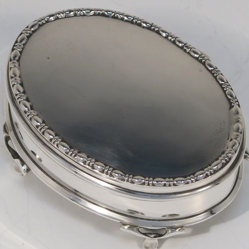 A very elegant Antique Sterling Silver jewelery box, having a plain oval-shaped body with straight sides, a slightly domed hinged lid with an applied pear and bead top border, a gold gilt and green velvet-lined interior, and all sitting on four flanged feet. This handsome silver jewellery box was made by Charles Edwards of London in 1918. The dimensions of this fine hand-made antique silver jewellery box are width 9 cms (3.5 inches), depth 6.5 cms (2.5 inches), and height 4.5 cms (1.75 inches)