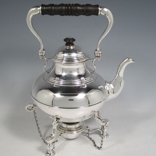 Sterling silver tea kettle on a burner stand, having a plain round baluster body with reeded decoration, a lift-off lid with wooden finial, a hinged handle with wooden insert, and sitting on an original burner stand with retaining pins and three cast hoof feet. Made by Robert Comyns of London in 1929. The dimensions of this fine silver kettle are length 21 cms (8.25 inches), height 28 cms (11 inches), width 14.5 cms (5.75 inches), and the total weight is approx. 1,000g (32 troy ounces).