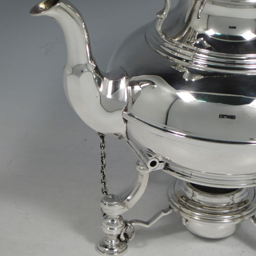 Sterling silver tea kettle on a burner stand, having a plain round baluster body with reeded decoration, a lift-off lid with wooden finial, a hinged handle with wooden insert, and sitting on an original burner stand with retaining pins and three cast hoof feet. Made by Robert Comyns of London in 1929. The dimensions of this fine silver kettle are length 21 cms (8.25 inches), height 28 cms (11 inches), width 14.5 cms (5.75 inches), and the total weight is approx. 1,000g (32 troy ounces).