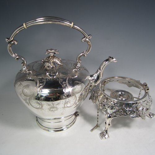 Antique Victorian silver-plated tea kettle on a burner stand, having a round baluster body with hand-engraved floral decoration, a hinged lid with flower finial, an insulated handle, and all sitting on an original burner stand with retaining pins and three cast feet. Made in ca. 1870. The dimensions of this fine silver-plated kettle are length 28 cms (11 inches), height 41 cms (16 inches), and width 20 cms (8 inches).