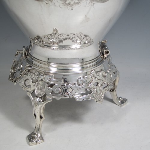 Antique Victorian silver-plated tea kettle on a burner stand, having a round baluster body with hand-engraved floral decoration, a hinged lid with flower finial, an insulated handle, and all sitting on an original burner stand with retaining pins and three cast feet. Made in ca. 1870. The dimensions of this fine silver-plated kettle are length 28 cms (11 inches), height 41 cms (16 inches), and width 20 cms (8 inches).
