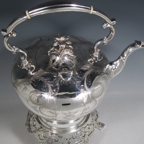 Antique Victorian silver-plated tea kettle on a burner stand, having a round baluster body with hand-engraved floral decoration, a hinged lid with flower finial, an insulated handle, and all sitting on an original burner stand with retaining pins and three cast feet. Made in ca. 1870. The dimensions of this fine silver-plated kettle are length 28 cms (11 inches), height 41 cms (16 inches), and width 20 cms (8 inches).