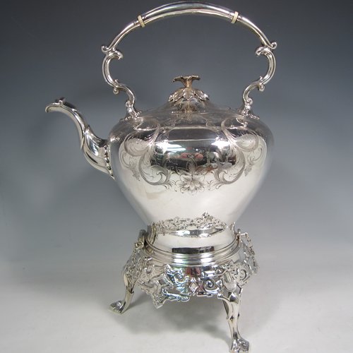 Antique Victorian silver-plated tea kettle on a burner stand, having a round baluster body with hand-engraved floral decoration, a hinged lid with flower finial, an insulated handle, and all sitting on an original burner stand with retaining pins and three cast feet. Made in ca. 1870. The dimensions of this fine silver-plated kettle are length 28 cms (11 inches), height 41 cms (16 inches), and width 20 cms (8 inches).