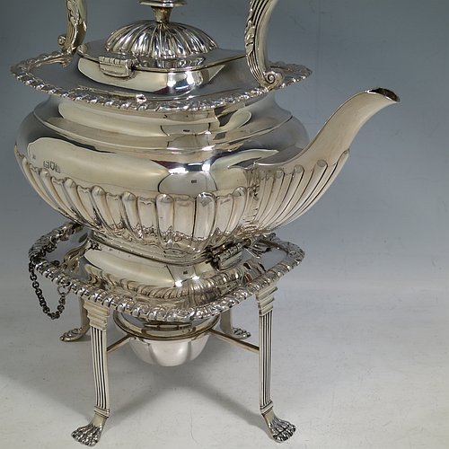 An Antique Victorian Sterling Silver tea kettle on a burner stand, having a Georgian Regency style rectangular bellied body with applied gadroon & shell borders and hand-chased fluted decoration, together with a hinged domed lid, an insulated silver handle and finial, and sitting on an original burner stand with four fluted lions-paw feet. Made by Charles Boyton of London in 1900. The dimensions of this fine hand-made antique silver kettle are length 24 cms (9.5 inches), height 33 cms (13 inches), width 15 cms (6 inches), and the total weight is approx. 1,056g (34 troy ounces).