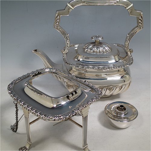 An Antique Victorian Sterling Silver tea kettle on a burner stand, having a Georgian Regency style rectangular bellied body with applied gadroon & shell borders and hand-chased fluted decoration, together with a hinged domed lid, an insulated silver handle and finial, and sitting on an original burner stand with four fluted lions-paw feet. Made by Charles Boyton of London in 1900. The dimensions of this fine hand-made antique silver kettle are length 24 cms (9.5 inches), height 33 cms (13 inches), width 15 cms (6 inches), and the total weight is approx. 1,056g (34 troy ounces).