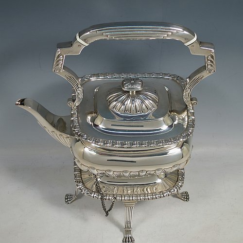 An Antique Victorian Sterling Silver tea kettle on a burner stand, having a Georgian Regency style rectangular bellied body with applied gadroon & shell borders and hand-chased fluted decoration, together with a hinged domed lid, an insulated silver handle and finial, and sitting on an original burner stand with four fluted lions-paw feet. Made by Charles Boyton of London in 1900. The dimensions of this fine hand-made antique silver kettle are length 24 cms (9.5 inches), height 33 cms (13 inches), width 15 cms (6 inches), and the total weight is approx. 1,056g (34 troy ounces).