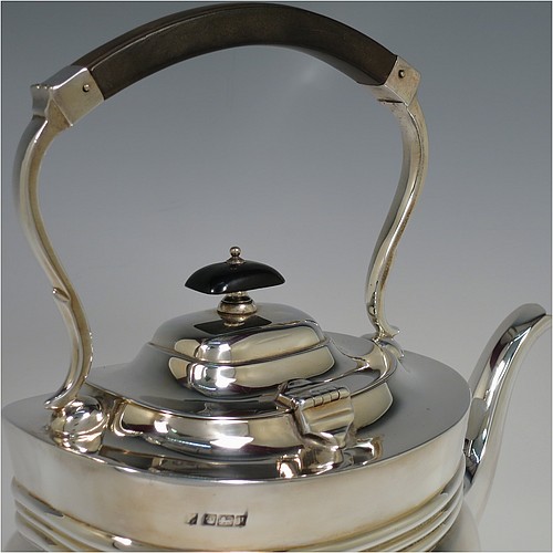 An Antique Edwardian Sterling Silver tea kettle on a burner stand, having a Georgian style rectangular baluster body, with a hinged domed lid, an insulated wooden handle and finial, and sitting on an original burner stand and four cast foliate feet. Made by Fordham and Faulkner of Sheffield in 1905. The dimensions of this fine hand-made antique silver kettle are length 23.5 cms (9.5 inches), height 33 cms (13 inches), width 15 cms (6 inches), and the total weight is approx. 1,350g (43.5 troy ounces).