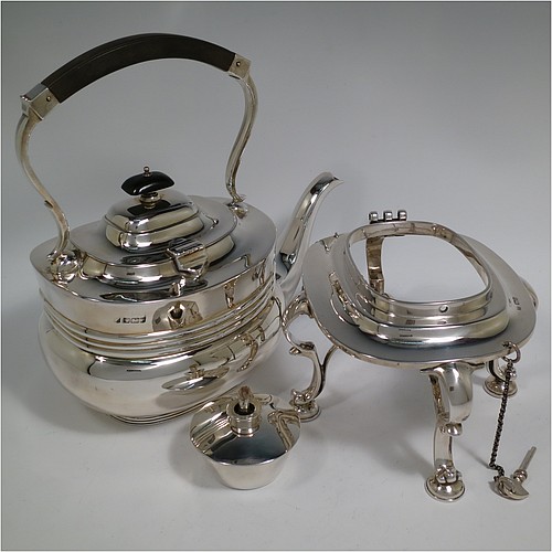 An Antique Edwardian Sterling Silver tea kettle on a burner stand, having a Georgian style rectangular baluster body, with a hinged domed lid, an insulated wooden handle and finial, and sitting on an original burner stand and four cast foliate feet. Made by Fordham and Faulkner of Sheffield in 1905. The dimensions of this fine hand-made antique silver kettle are length 23.5 cms (9.5 inches), height 33 cms (13 inches), width 15 cms (6 inches), and the total weight is approx. 1,350g (43.5 troy ounces).