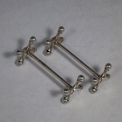 An Antique Edwardian Sterling Silver pair of knife rests, with traditional cast Jack-style rest ends, and plain round central struts. Made by William Hutton & Sons of Sheffield in 1910. The dimensions of this fine hand-made pair of antique silver knife rests are length 8 cms (3 inches), height 3 cms (1.25 inches), and they weigh a total of approx. 101g (3.3 troy ounces).