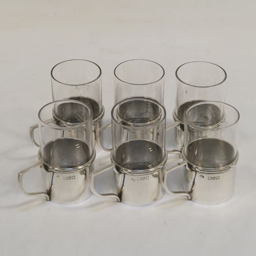A handsome Antique Edwardian Sterling Silver and cut-glass set of six liqueor tots or measures, having plain round bodies with scroll side-handles and applied ribbon and reed top borders, and plain round glass inserts with star-cut bases. These elegant silver and cut-glass liquor tots were made by William Comyns of London in 1906. The dimensions of this fine hand-made antique silver liqueur tot set are height 5 cms (2 inches), diameter 3 cms (1.25 inches), and their total weight is approx. 84g (2.7 troy ounces). Please note that these are part-crested.