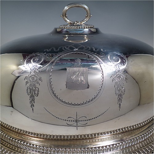 An Antique Georgian Old Sheffield plated meat cover dome and warming stand platter, having a plain oval body with Regency style gadroon and fluted border, a cast reeded loop handle, and all sitting on a well and tree dish for carving, having a hot water jacket, and with matching decoration, and sitting on four cushion feet. Made in the Regency period ca. 1815. The dimensions of this fine hand-made Old Sheffield plated meat cover dome and hot water stand are length (inc. handles) 53 cm (21 inches), width 42 cms (16.5 inches), and height 34 cms (13.5 inches). Please note that the meat dome is engraved and crested on one side.