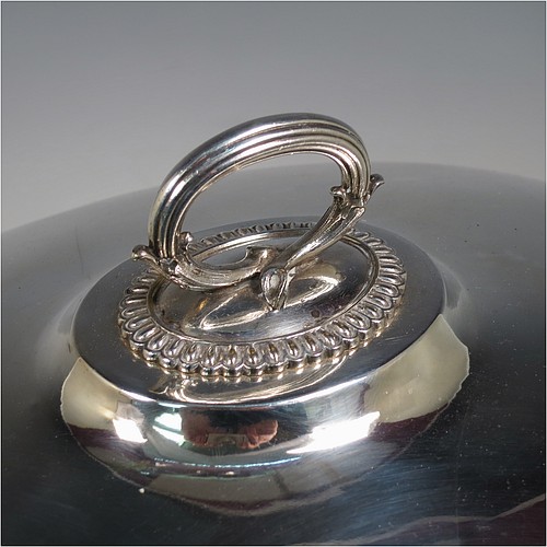 An Antique Georgian Old Sheffield plated meat cover dome and warming stand platter, having a plain oval body with Regency style gadroon and fluted border, a cast reeded loop handle, and all sitting on a well and tree dish for carving, having a hot water jacket, and with matching decoration, and sitting on four cushion feet. Made in the Regency period ca. 1815. The dimensions of this fine hand-made Old Sheffield plated meat cover dome and hot water stand are length (inc. handles) 53 cm (21 inches), width 42 cms (16.5 inches), and height 34 cms (13.5 inches). Please note that the meat dome is engraved and crested on one side.