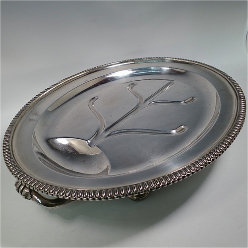 An Antique Georgian Old Sheffield plated meat cover dome and warming stand platter, having a plain oval body with Regency style gadroon and fluted border, a cast reeded loop handle, and all sitting on a well and tree dish for carving, having a hot water jacket, and with matching decoration, and sitting on four cushion feet. Made in the Regency period ca. 1815. The dimensions of this fine hand-made Old Sheffield plated meat cover dome and hot water stand are length (inc. handles) 53 cm (21 inches), width 42 cms (16.5 inches), and height 34 cms (13.5 inches). Please note that the meat dome is engraved and crested on one side.