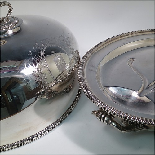 An Antique Georgian Old Sheffield plated meat cover dome and warming stand platter, having a plain oval body with Regency style gadroon and fluted border, a cast reeded loop handle, and all sitting on a well and tree dish for carving, having a hot water jacket, and with matching decoration, and sitting on four cushion feet. Made in the Regency period ca. 1815. The dimensions of this fine hand-made Old Sheffield plated meat cover dome and hot water stand are length (inc. handles) 53 cm (21 inches), width 42 cms (16.5 inches), and height 34 cms (13.5 inches). Please note that the meat dome is engraved and crested on one side.