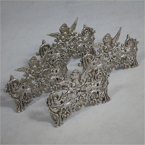 An Antique Sterling Silver set of four place card holders, having cast bodies with winged seraphims over scroll and floral decoration, and sitting on half-circle wire-work bases. Made by Stuart Clifford of London in 1904. The dimensions of this fine set of antique silver place card holders are width 7.5 cms (3 inches), height 5 cms (2 inches), depth 4 cms (1.5 inches), and they weigh a total of approx. 101g (3.3 troy ounces).    
