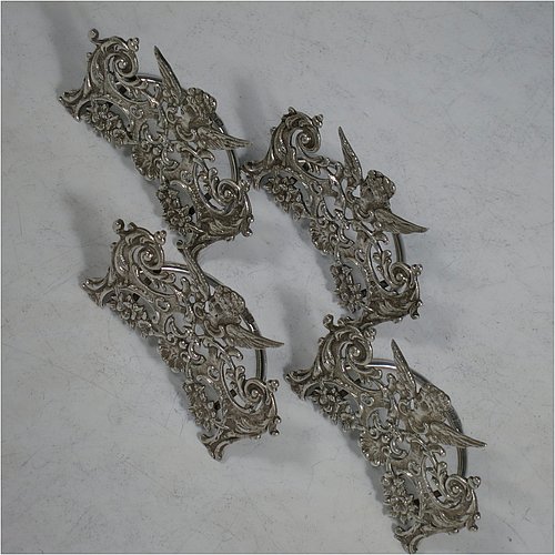 An Antique Sterling Silver set of four place card holders, having cast bodies with winged seraphims over scroll and floral decoration, and sitting on half-circle wire-work bases. Made by Stuart Clifford of London in 1904. The dimensions of this fine set of antique silver place card holders are width 7.5 cms (3 inches), height 5 cms (2 inches), depth 4 cms (1.5 inches), and they weigh a total of approx. 101g (3.3 troy ounces).