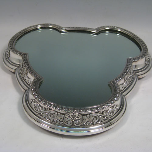 Antique Victorian silver-plated mirror plateau, having a very unusual tri-lobed shaped body, applied floral and scroll borders, and an original oak base with three hinged feet for ease of cleaning. Made by Elkington and Co., with their date letter for 1873. The dimensions of this fine hand-made mirror plateau are width 34 cms (13.5 inches), and height 5 cms (2 inches).   