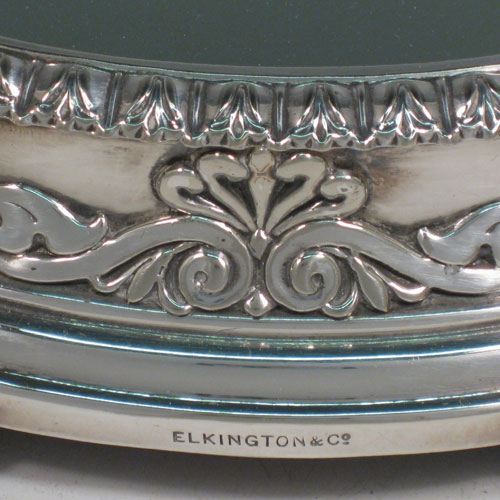 Antique Victorian silver-plated mirror plateau, having a very unusual tri-lobed shaped body, applied floral and scroll borders, and an original oak base with three hinged feet for ease of cleaning. Made by Elkington and Co., with their date letter for 1873. The dimensions of this fine hand-made mirror plateau are width 34 cms (13.5 inches), and height 5 cms (2 inches).