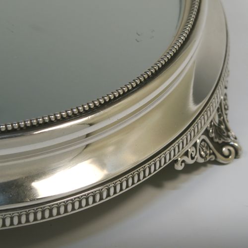 A very pretty Antique Victorian Sterling Silver mirror plateau, having a round body with an applied bead-edged top border surrounding the mirror, an applied gadroon-edged bottom border, all sitting on three cast foliate and shell feet, and an original oak base underneath. This elegant antique silver mirror plateau was made by Henry Woodward of Birmingham in 1876. The dimensions of this fine hand-made antique silver mirror plateau are diameter 29 cms (11.5 inches), and height 6 cms (2.3 inches).