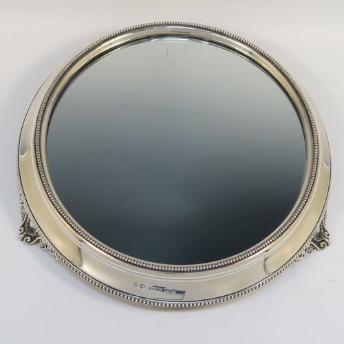 A very pretty Antique Victorian Sterling Silver mirror plateau, having a round body with an applied bead-edged top border surrounding the mirror, an applied gadroon-edged bottom border, all sitting on three cast foliate and shell feet, and an original oak base underneath. This elegant antique silver mirror plateau was made by Henry Woodward of Birmingham in 1876. The dimensions of this fine hand-made antique silver mirror plateau are diameter 29 cms (11.5 inches), and height 6 cms (2.3 inches).