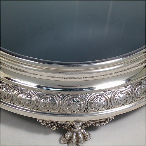 An Antique Edwardian Sterling Silver mirror plateau, having a round body with hand-chased floral decoration, a plain reeded border surrounding the mirror, all sitting on three cast foliate and lions-paw feet, and an original oak base underneath. Made by the Deakin Brothers of Sheffield in 1904. The dimensions of this fine hand-made antique silver mirror plateau are diameter 38 cms (15 inches), and height 9 cms (3.5 inches).
