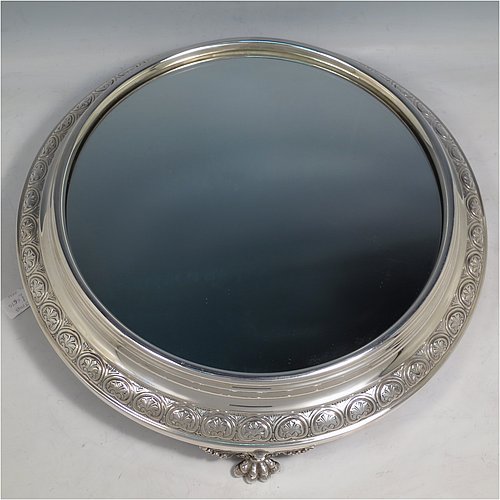 An Antique Edwardian Sterling Silver mirror plateau, having a round body with hand-chased floral decoration, a plain reeded border surrounding the mirror, all sitting on three cast foliate and lions-paw feet, and an original oak base underneath. Made by the Deakin Brothers of Sheffield in 1904. The dimensions of this fine hand-made antique silver mirror plateau are diameter 38 cms (15 inches), and height 9 cms (3.5 inches).