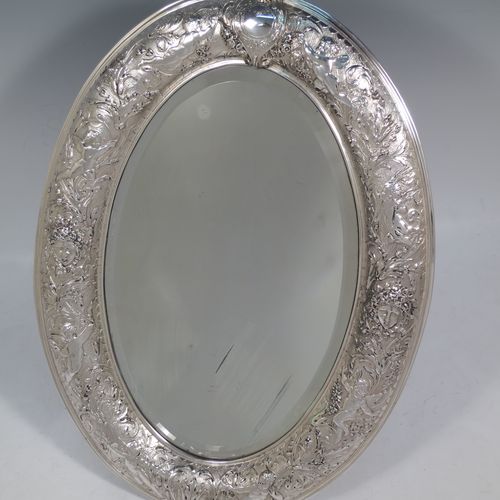 A very unusual and pretty Antique Victorian Sterling Silver table or vanity mirror (that also doubles as a mirror plateau), having hand-chased cherubs and floral work, surrounding an original bevelled oval mirror, and a blue velvet backing with eight stud feet and an easel stand. Made by Elkington and Co., of Birmingham in 1900. The dimensions across the frame of this fine hand-made antique silver vanity or table mirror are height 38 cms (15 inches), and width 27 cms (10.5 inches). Please note that the silver backing to the mirror has age-related marks, but nothing too serious.   