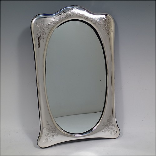 A very pretty Antique Edwardian Sterling Silver table or vanity mirror having hand-engraved floral work with ribbon and bow decoration, surrounding an oval mirror, and a blue velvet backing with easel stand. Made by the Alexander Clark Manufacturing Company of Birmingham in 1910. The dimensions across the frame of this fine hand-made antique silver vanity or table mirror are height 33 cms (13 inches), and width 21 cms (8.25 inches).   