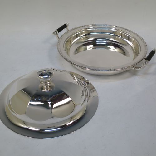 A handsome Antique Sterling Silver muffin dish, having a round body with an applied ribbon and reed border, with two side handles having black ebonised inserts, a domed and panelled lift-off lid with cast finial, and all sitting on a flat base. Made by James Dixon and Sons of Sheffield in 1911. The dimensions of this fine hand-made antique silver muffin dish are diameter 18 cms (7 inches), height 9 cms (3.5 inches), and it weighs approx. 330g (10.6 troy ounces).