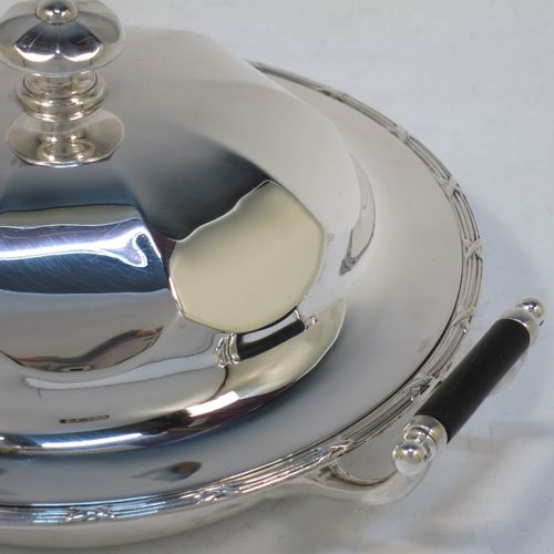 A handsome Antique Sterling Silver muffin dish, having a round body with an applied ribbon and reed border, with two side handles having black ebonised inserts, a domed and panelled lift-off lid with cast finial, and all sitting on a flat base. Made by James Dixon and Sons of Sheffield in 1911. The dimensions of this fine hand-made antique silver muffin dish are diameter 18 cms (7 inches), height 9 cms (3.5 inches), and it weighs approx. 330g (10.6 troy ounces).