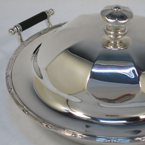 A handsome Antique Sterling Silver muffin dish, having a round body with an applied ribbon and reed border, with two side handles having black ebonised inserts, a domed and panelled lift-off lid with cast finial, and all sitting on a flat base. Made by James Dixon and Sons of Sheffield in 1911. The dimensions of this fine hand-made antique silver muffin dish are diameter 18 cms (7 inches), height 9 cms (3.5 inches), and it weighs approx. 330g (10.6 troy ounces).