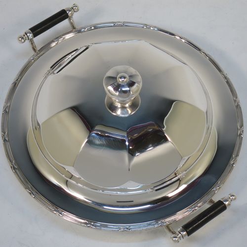 A handsome Antique Sterling Silver muffin dish, having a round body with an applied ribbon and reed border, with two side handles having black ebonised inserts, a domed and panelled lift-off lid with cast finial, and all sitting on a flat base. Made by James Dixon and Sons of Sheffield in 1911. The dimensions of this fine hand-made antique silver muffin dish are diameter 18 cms (7 inches), height 9 cms (3.5 inches), and it weighs approx. 330g (10.6 troy ounces).