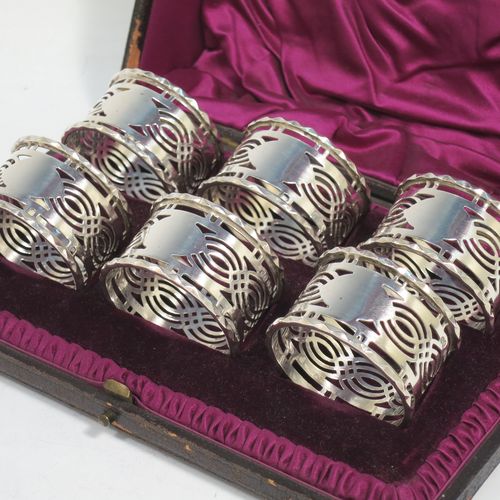 A pretty Antique Sterling Silver set of six napkin rings, having round straight-sided bodies, with hand-pierced geometrical style decoration, a central oval vacant cartouche, and with applied faceted borders, all in their original maroon satin and velvet-lined presentation box. Made by Ferganbaum and Son of Birmingham in 1921. The dimensions of these fine hand-made silver napkin rings are diameter 4.5 cms (1.75 inches), height 2.5 cms (1 inch), and they weigh a total of approx. 140g (4.5 troy ounces).