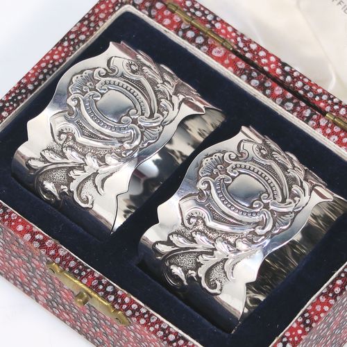 A very pretty Antique Victorian Sterling Silver pair of napkin rings, having round straight-sided bodies with hand-chased floral and scroll decoration surrounding an oval vacant cartouche on one side, all in their original cream satin and dark blue velvet-lined presentation box. These beautiful antique silver napkin rings were made by George Maudsley Jackson of London in 1898. The dimensions of these fine hand-made antique silver napkin rings are diameter 4.5 cms (1.75 inches), height 3 cms (1 inches), and they weigh a total of approx. 56g (1.8 troy ounces).