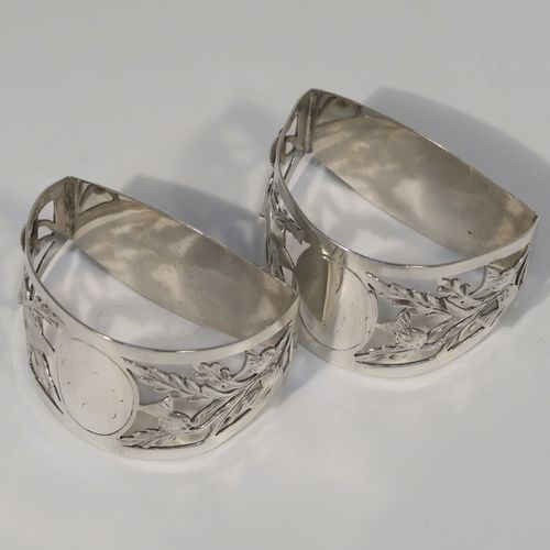 A very pretty Antique Art Nouveau style Sterling Silver pair of napkin rings, having semi-circular bodies with flat sides, with hand-pierced Scottish Thistle floral decoration, surrounding vacant oval cartouches. These beautiful antique silver napkin rings were made by Walker and Hall of Sheffield in 1911. The dimensions of these fine hand-made antique silver napkin rings are length 5 cms (2 inches), height 3.5 cms (1.3 inches), and they weigh a total of approx. 56g (1.8 troy ounces).