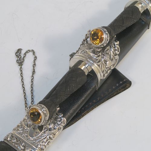 A beautiful and large sterling silver, black leather, and carved wooden Scottish Dirk holder, having hand-chased silver mounts with thistle decoration, carved hard-wood handles, a leather scabbard, smoky Citreen handle tops, removable main knife, eating knife and fork with stainless steel blades and security chains, and a black leather belt loop. This handsome silver, wood, and leather Dirk holder was made by Anthony Holland of Edinburgh in 1978. The dimensions of this fine hand-made Scottish sterling silver Dirk holder are lenght 49 cms (19.25 inches) and width 5 cms (2 inches).