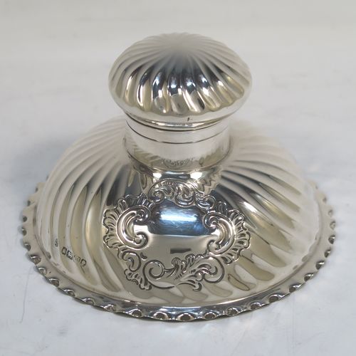A very pretty Antique Victorian Sterling Silver desk set consisting of an inkstand and a pair of candle holders, in a round style with hand-chased swirl fluting and wavy-edge borders, the inkstand with a hinged lid and glass liner, the candlesticks with removable nozzles. This beautiful silver desk set was made by the Dixon Brothers of Sheffield in 1889. The dimensions of this fine antique silver desk set are height of candlesticks 14 cms (5.5 inches), and diameter of inkstand at base 11.5 cms (4.5 inches).