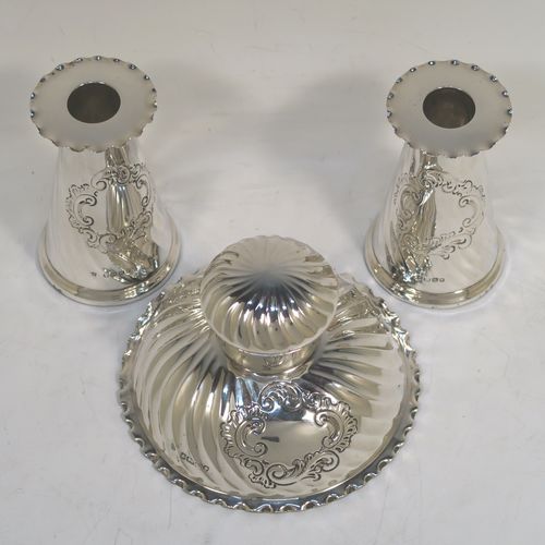 A very pretty Antique Victorian Sterling Silver desk set consisting of an inkstand and a pair of candle holders, in a round style with hand-chased swirl fluting and wavy-edge borders, the inkstand with a hinged lid and glass liner, the candlesticks with removable nozzles. This beautiful silver desk set was made by the Dixon Brothers of Sheffield in 1889. The dimensions of this fine antique silver desk set are height of candlesticks 14 cms (5.5 inches), and diameter of inkstand at base 11.5 cms (4.5 inches).